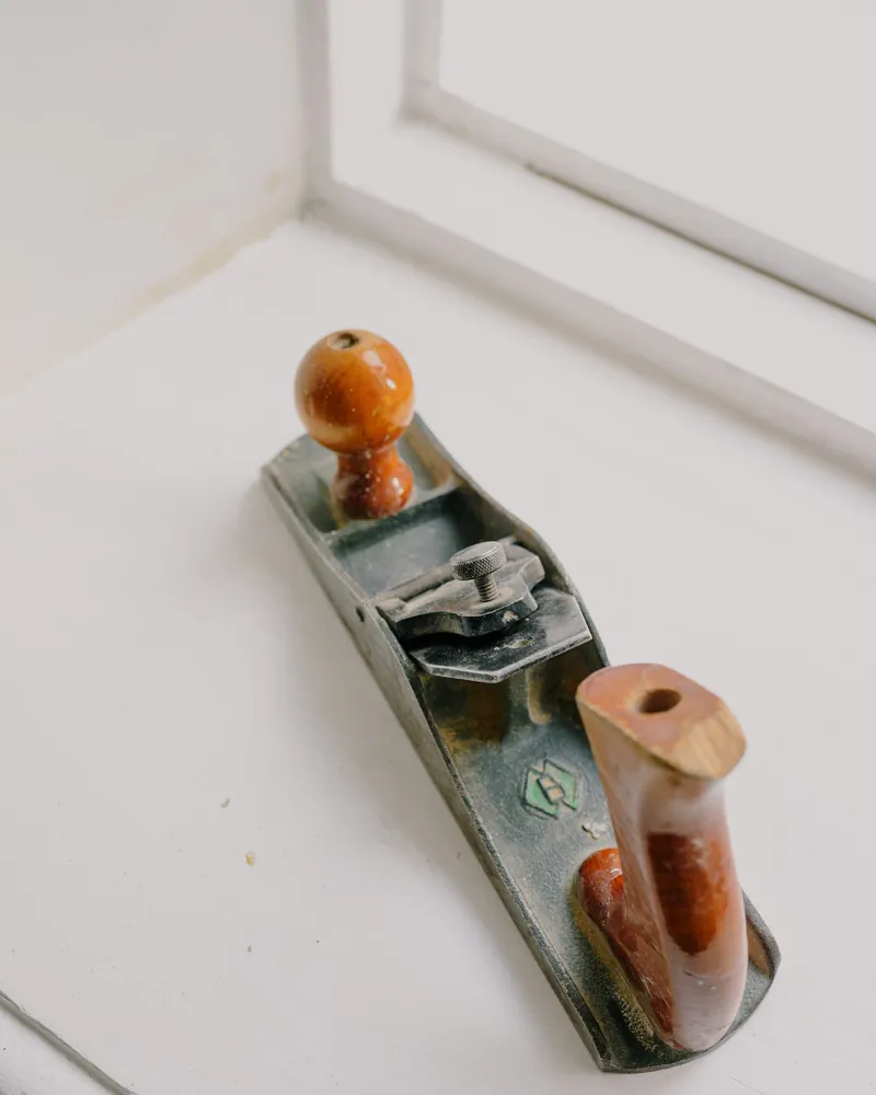 Cepillo de banco de fuste metálico con pomo de madera apoyado junto a una ventana