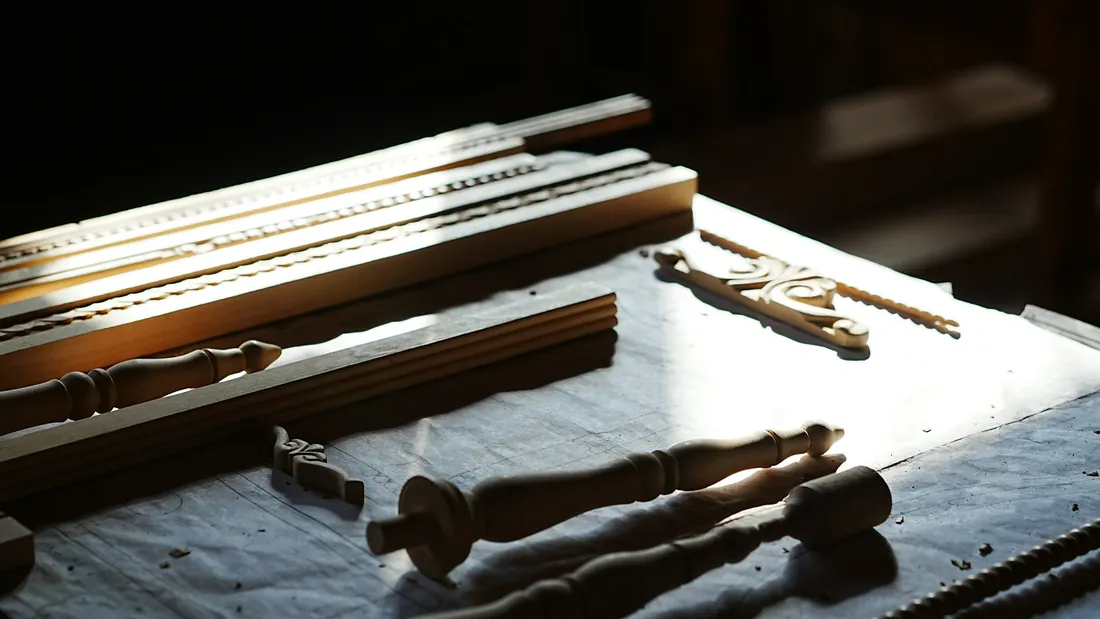 Piezas de madera talladas y herramientas de mano sobre un banco de taller iluminado por luz natural